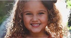Little girl with curly hair smiling outdoors