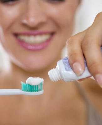 A woman applying toothpaste to an electric toothbrush