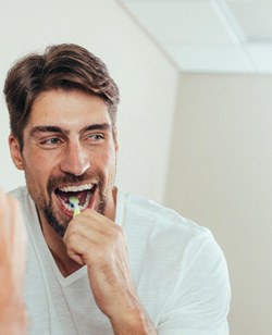 Man smiling while brushing his teeth in bathroom
