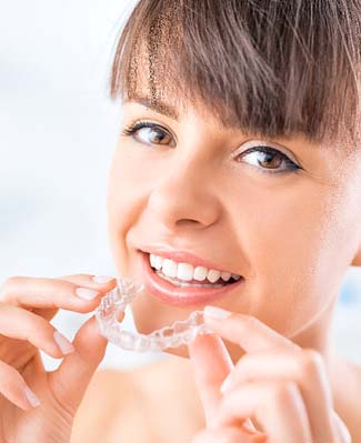 Closeup of woman smiling while putting in her Invisalign aligner