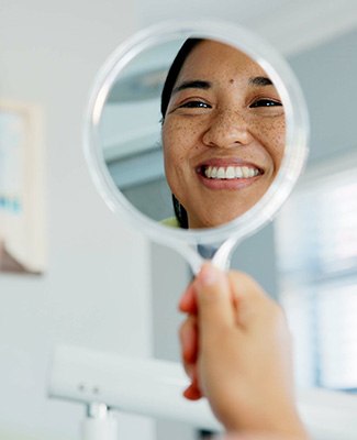 Woman smiling at reflection in handheld mirror
