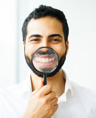 man in white dress shirt holding magnifying glass to his smile 