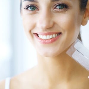 Woman holding up set of teeth whitening strips