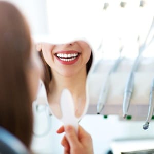 Woman using mirror to admire results of teeth whitening